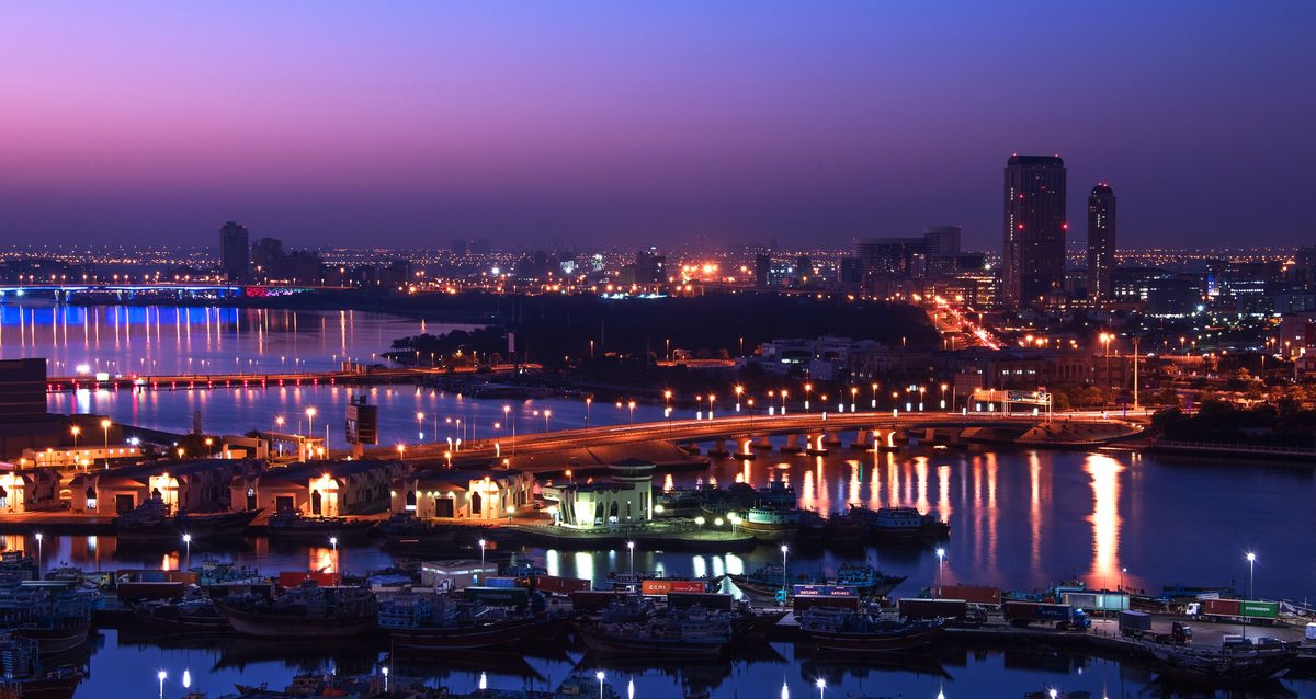 Dubai Creek at twilight: a bridge, moored boats, the low skyline reflected in the water