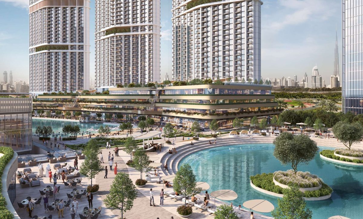 Sobha Hartland II from the air: the lagoon and retail spine in front, the tower cluster behind, Downtown Dubai on the horizon