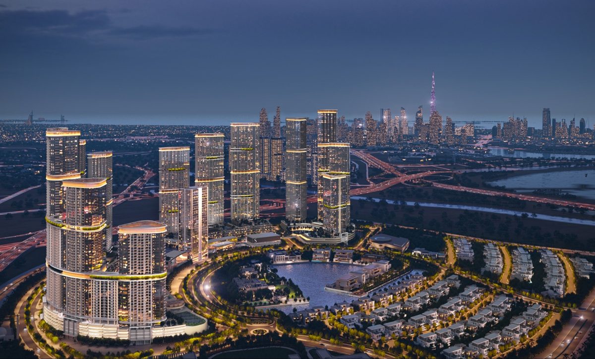 Sobha Hartland II after dark: the towers lit, the lagoon crescent glowing, Downtown Dubai on the horizon