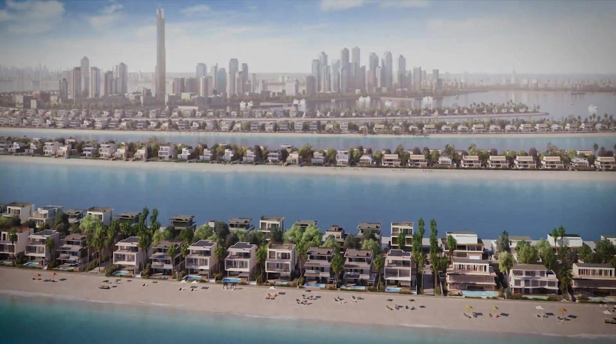 Low aerial along one frond of Palm Jebel Ali, villa rows on both sides, the Dubai Marina skyline on the horizon — a frame of Nakheel's own film