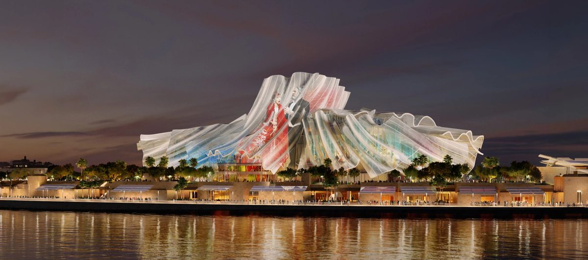 Dar Al Funoon, a performing-arts venue with a sculpted fabric-like facade, lit at dusk beside the waterfront promenade