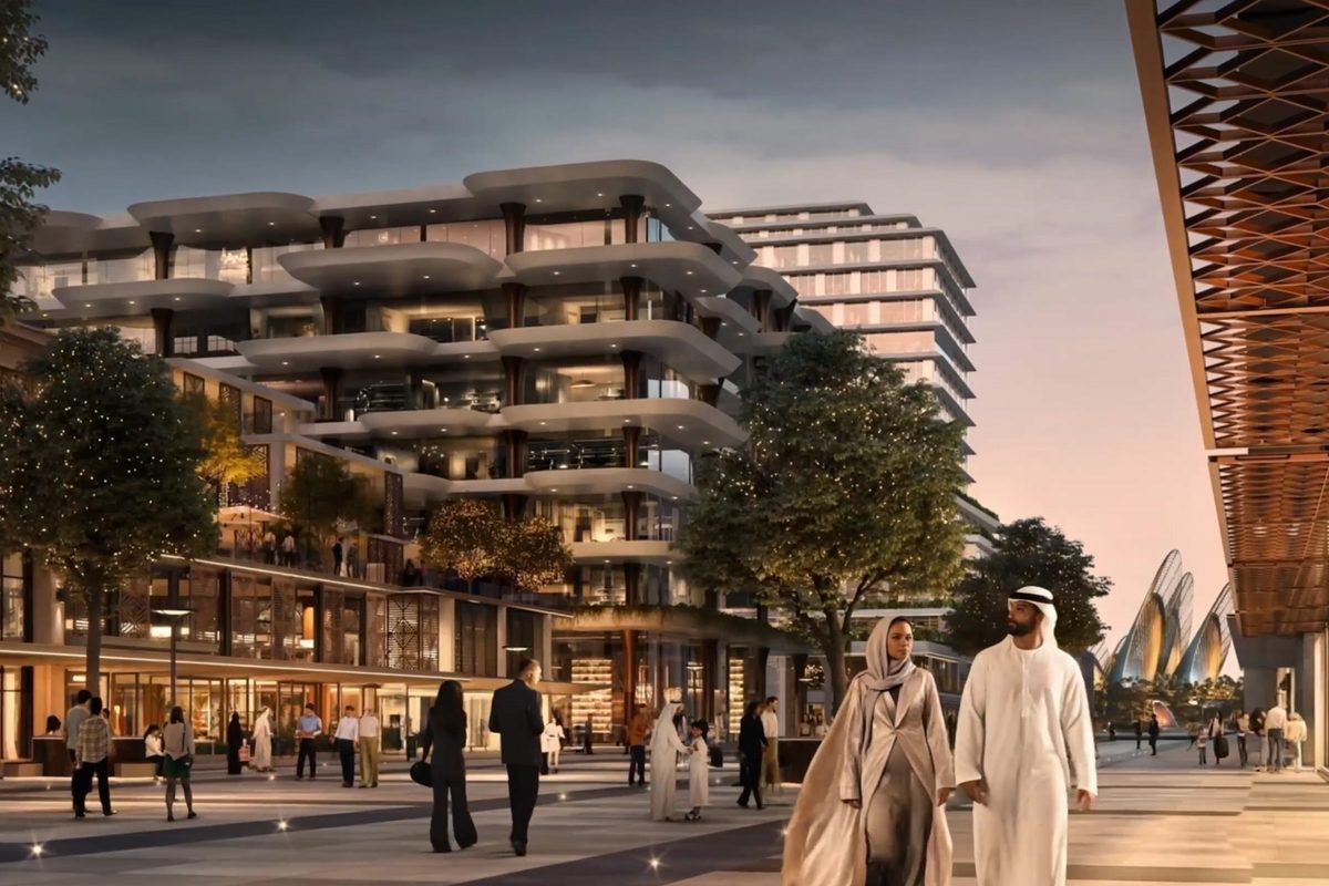 A residential building with rounded balconies above a lit retail colonnade at dusk, people walking the promenade